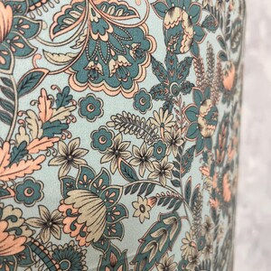Pode incluir: Close-up de um tecido com um design floral paisley. O padr&atilde;o apresenta flores e folhas verde-azuis, p&ecirc;ssego e bege sobre um fundo azul claro. O design &eacute; detalhado e intrincado, com uma est&eacute;tica vintage.
