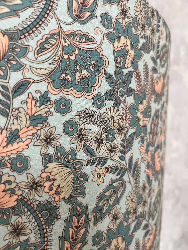 Pode incluir: Close-up de um tecido com um design floral paisley. O padr&atilde;o apresenta flores e folhas verde-azuis, p&ecirc;ssego e bege sobre um fundo azul claro. O design &eacute; detalhado e intrincado, com uma est&eacute;tica vintage.