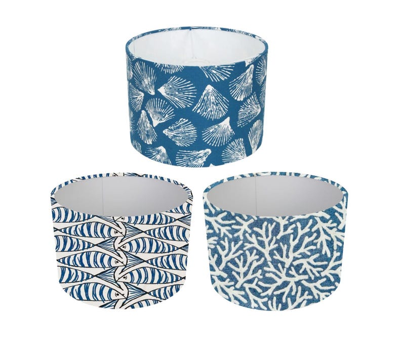 May include: Three lampshades featuring different blue and white nautical designs. The lampshades are cylindrical and have a white interior. The patterns include seashells, fish, and coral.