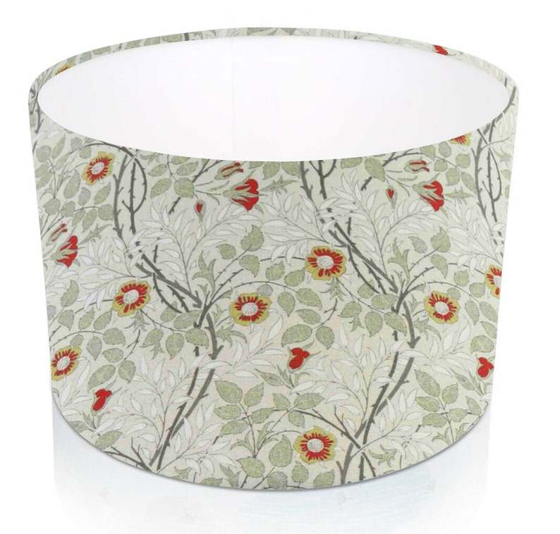 Pode incluir: Abajur cil&iacute;ndrico com um padr&atilde;o floral de flores vermelhas e amarelas, folhas verdes e caules cinzentos sobre um fundo creme. O interior &eacute; branco. Adequado para candeeiros de mesa ou de p&eacute;.