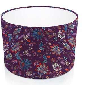 Pode incluir: Abajur cil&iacute;ndrico com um padr&atilde;o floral. A sombra apresenta um fundo roxo escuro com um design repetido de flores estilizadas em tons de verde-azulado, vermelho e branco. O interior &eacute; branco.