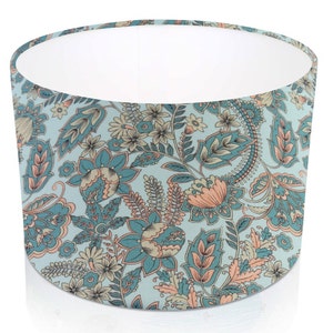 Pode incluir: Abajur cil&iacute;ndrico com um padr&atilde;o floral. O design apresenta flores e folhagens em tons de azul-petr&oacute;leo, p&ecirc;ssego e creme sobre um fundo azul claro. O interior do abajur &eacute; branco.