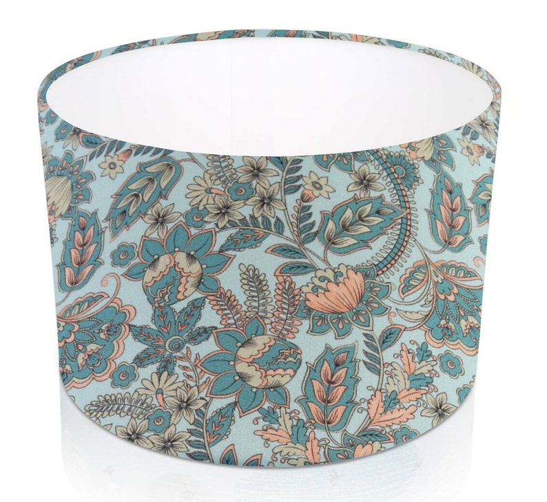 Pode incluir: Abajur cil&iacute;ndrico com um padr&atilde;o floral. O design apresenta flores e folhagens em tons de azul-petr&oacute;leo, p&ecirc;ssego e creme sobre um fundo azul claro. O interior do abajur &eacute; branco.