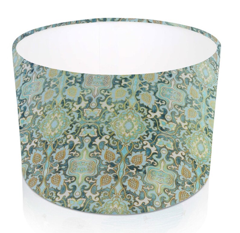 Pode incluir: Abajur cil&iacute;ndrico com um padr&atilde;o floral detalhado em tons de turquesa, azul e dourado. O interior &eacute; branco, contrastando com o design intrincado. O abajur foi projetado para difundir a luz.