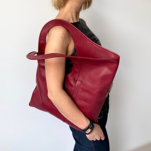 Burgundy leather bag has a rectangular shape. It is finished with an outside vertical zipper pocket. Height 17.5, Width 15.5 inches. The bag is fully lined and has two interior pockets. It can be carried on a shoulder or as a folded clutch.