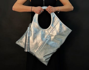 May include: A silver metallic tote bag with a large oval handle and a tassel. The bag has a zipper closure and a small pocket on the front.