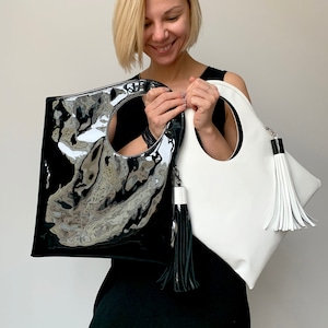 Black patent leather bag is finished with an outside vertical zipper pocket and a strap. The bag is fully lined and has two inner pockets. The bag can be carried on the shoulder or crossbody. Height 15 Width 13.5 inches.