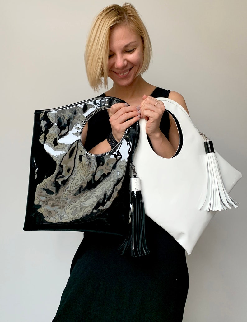 Black patent leather bag is finished with an outside vertical zipper pocket and a strap. The bag is fully lined and has two inner pockets. The bag can be carried on the shoulder or crossbody. Height 15 Width 13.5 inches.
