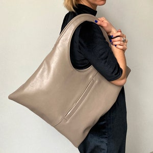 Taupe leather shoulder bag is finished with an outside vertical zipper pocket. The bag is fully lined and has two inner pockets. The bag can be carried on the shoulder or as a clutch. Height 17.5 Width 15.5 inches.