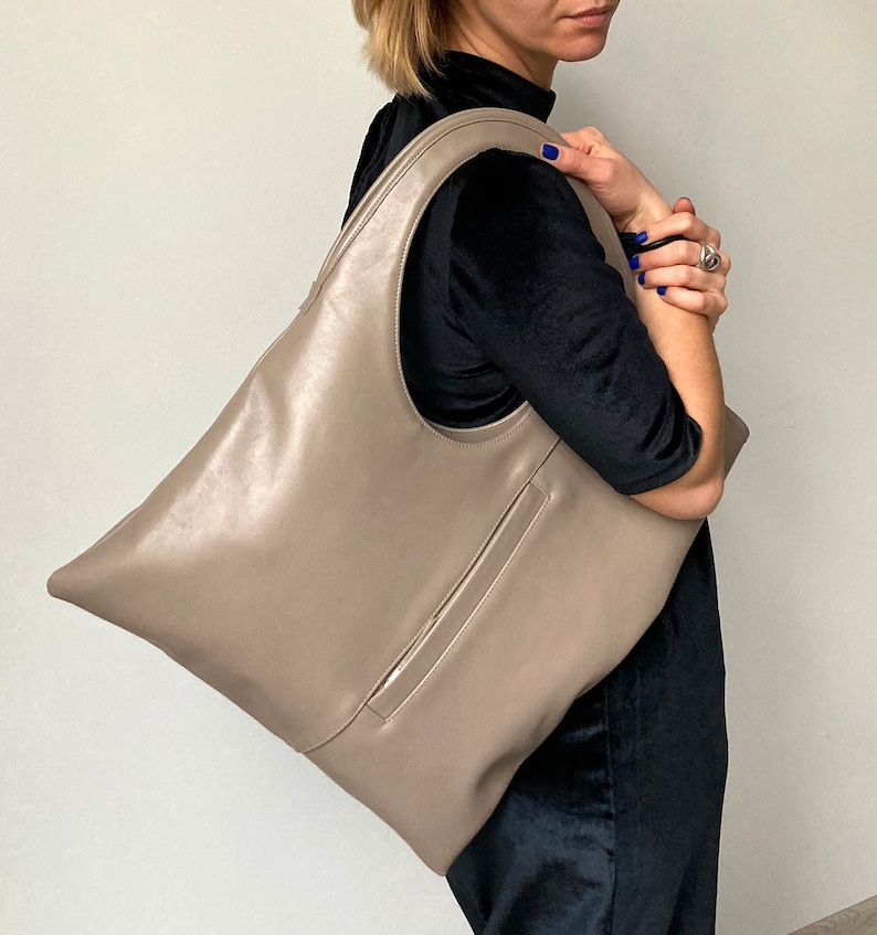 Taupe leather shoulder bag is finished with an outside vertical zipper pocket. The bag is fully lined and has two inner pockets. The bag can be carried on the shoulder or as a clutch. Height 17.5 Width 15.5 inches.