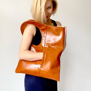 Cognac leather bag is finished with an outside vertical zipper pocket and a strap. The bag is fully lined and has two inner pockets. The bag can be carried on the shoulder or crossbody. Height 17.5 Width 15.5 inches.