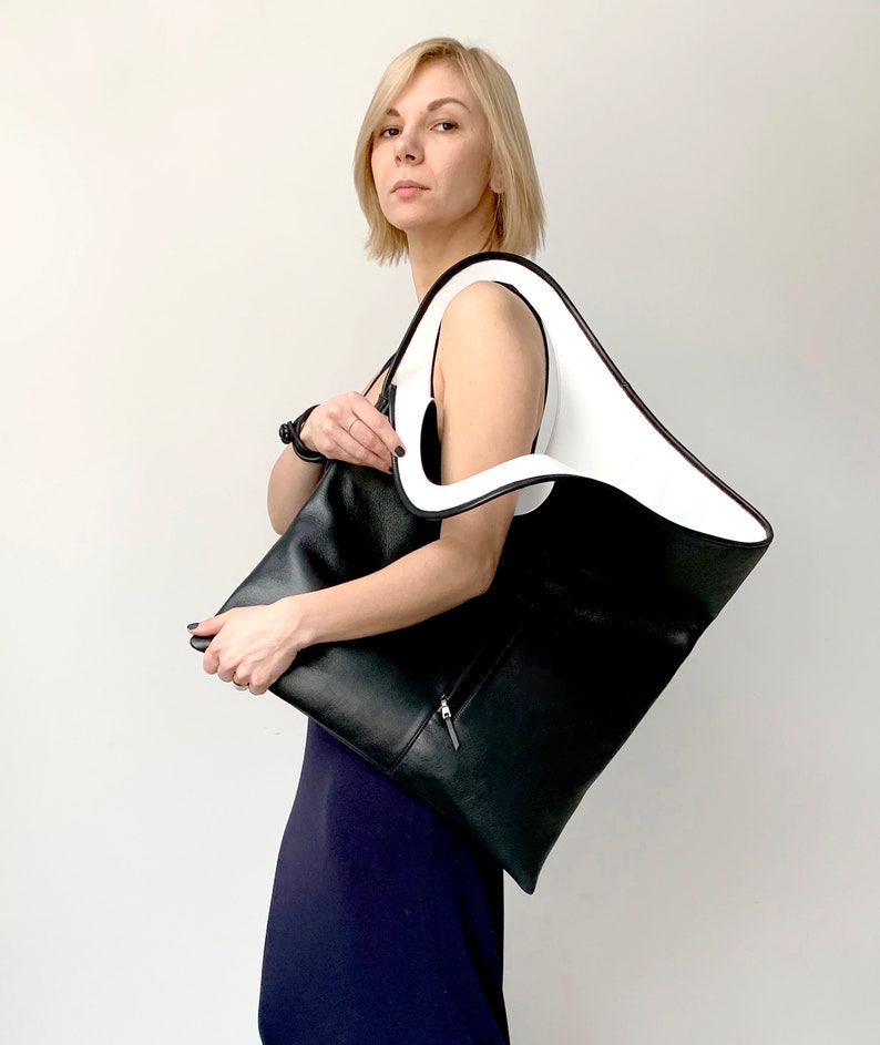 Black leather shoulder bag with white leather interior collar is finished with an outside vertical zipper pocket. The bag is fully lined and has two inner pockets. The bag can be carried on the shoulder or as a clutch. Height 20.5 Width 18.5 inches.