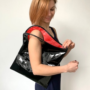 Black patent leather bag is finished with an outside vertical zipper pocket and a strap. The bag is fully lined and has two inner pockets. The bag can be carried on the shoulder or crossbody. Height 15 Width 13.5 inches.