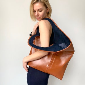 Brown leather shoulder bag with blue suede interior collar is finished with an outside vertical zipper pocket. The bag is fully lined and has two inner pockets. The bag can be carried on the shoulder or as a clutch. Height 19 Width 17 inches.