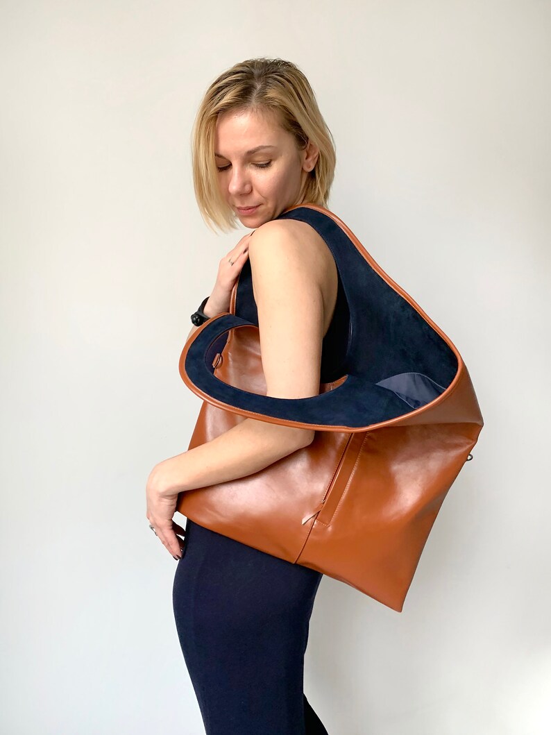 Brown leather shoulder bag with blue suede interior collar is finished with an outside vertical zipper pocket. The bag is fully lined and has two inner pockets. The bag can be carried on the shoulder or as a clutch. Height 19 Width 17 inches.