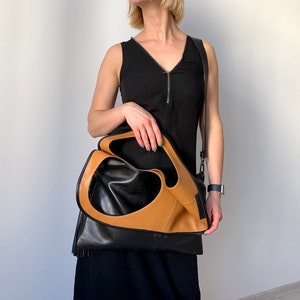 Black leather shoulder bag with tan leather interior collar. The bag has an outside vertical zipped pocket. The purse is carried as a folded over crossbody bag. It also can be carried in hand as a tote, over the shoulder or as a fold over clutch.