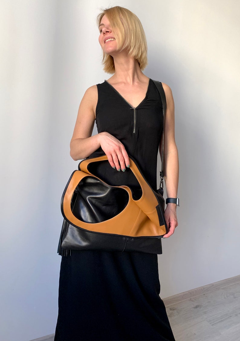 Black leather shoulder bag with tan leather interior collar. The bag has an outside vertical zipped pocket. The purse is carried as a folded over crossbody bag. It also can be carried in hand as a tote, over the shoulder or as a fold over clutch.