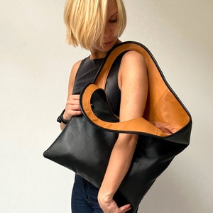 Black leather shoulder bag with tan interior collar is finished with an outside vertical zipper pocket. The bag is fully lined and has two inner pockets. The bag can be carried on the shoulder or as a clutch. Height 19 Width 17 inches.