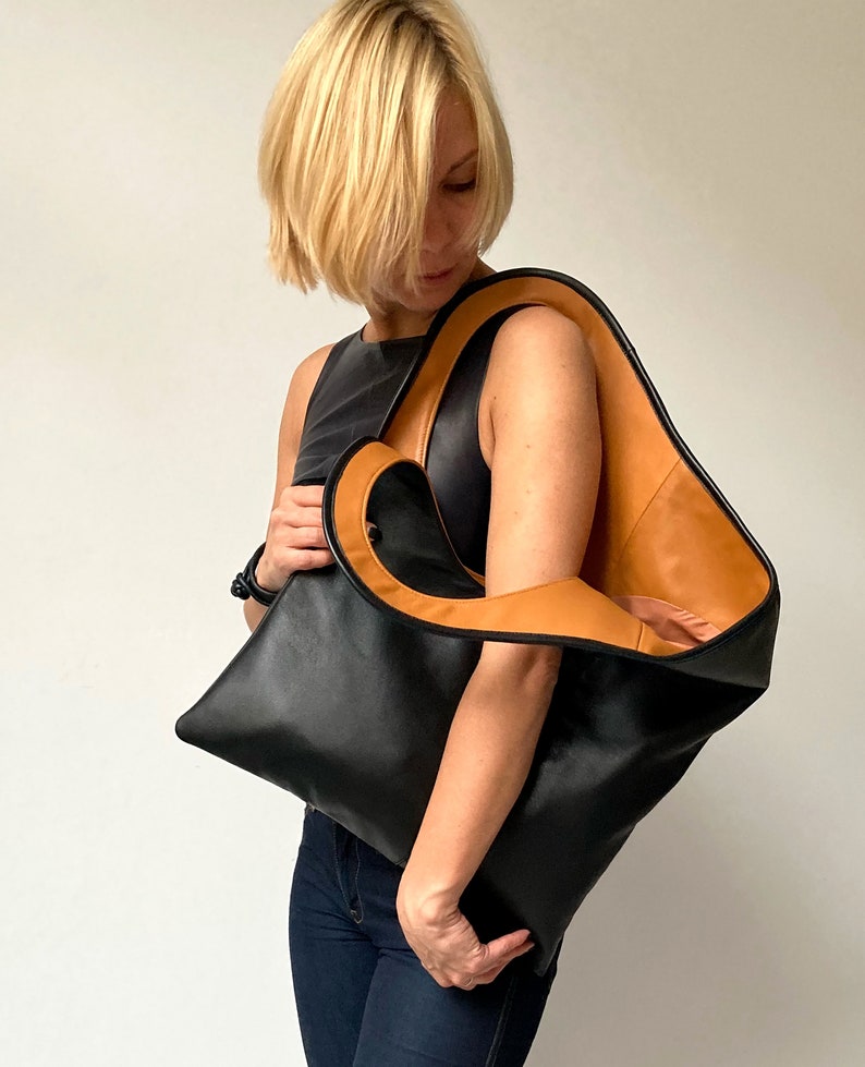 Black leather shoulder bag with tan interior collar is finished with an outside vertical zipper pocket. The bag is fully lined and has two inner pockets. The bag can be carried on the shoulder or as a clutch. Height 19 Width 17 inches.