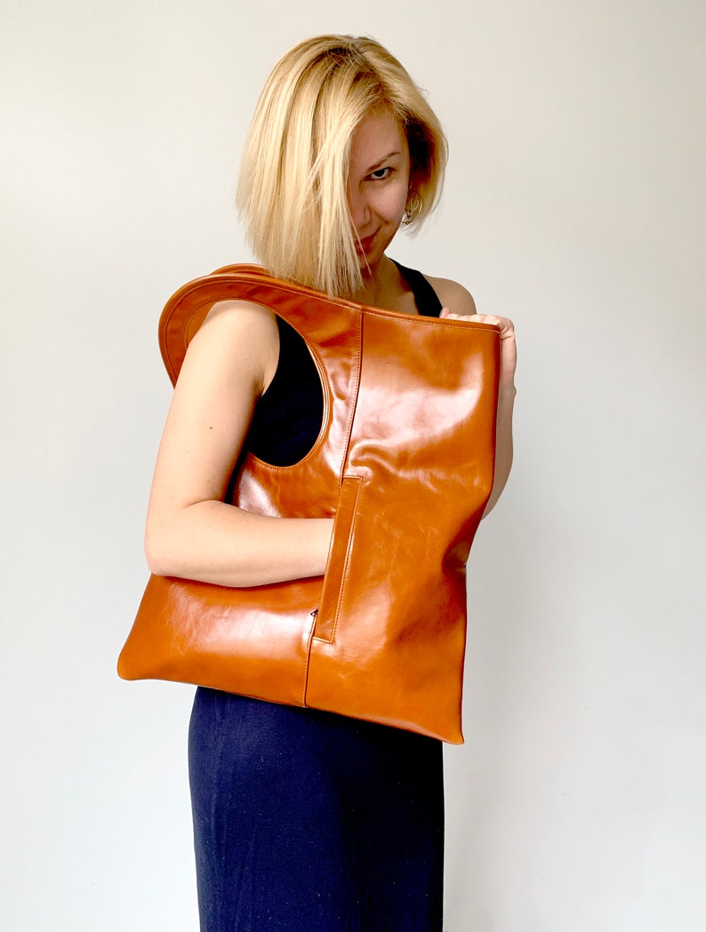 Cognac leather hobo bag finished with a side vertical zipped pocket. It has a rectangular shape. Size 19/17inches. The bag can be carried in hand as a tote, over the shoulder or as a fold over clutch. It is fully lined with two inside pockets.