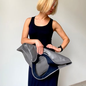Grey leather bag is finished with an outside vertical zipper pocket and a strap. The bag is fully lined and has two inner pockets. The bag can be carried on the shoulder or crossbody. Height 17.5 Width 15.5 inches.