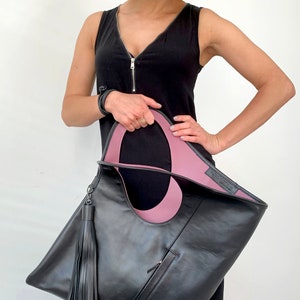 Black leather bag with pink interior collar. Size: hight 19 width 17 inches. It is finished with an outside vertical zipper pocket. The bag is fully lined and has two inner pockets. The bag can be carried either on a shoulder or as a foldover clutch.