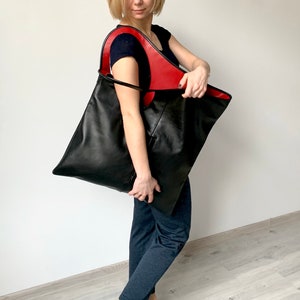 Black leather shoulder bag with red interior collar is finished with an outside vertical zipper pocket. The bag is fully lined and has two inner pockets. The bag can be carried on the shoulder or as a clutch. Height 22 Width 20 inches.