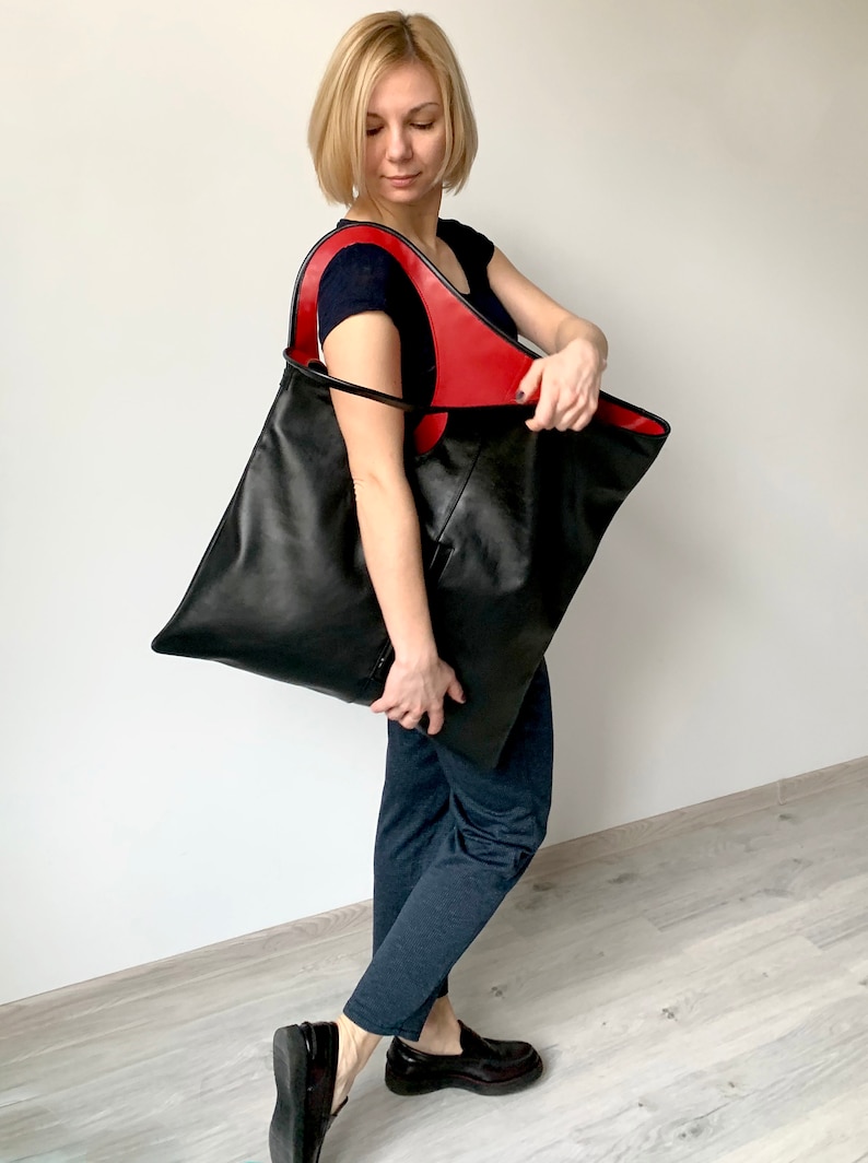 Black leather shoulder bag with red interior collar is finished with an outside vertical zipper pocket. The bag is fully lined and has two inner pockets. The bag can be carried on the shoulder or as a clutch. Height 22 Width 20 inches.
