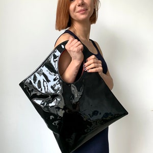 Black patent leather bag is finished with an outside vertical zipper pocket and a strap. The bag is fully lined and has two inner pockets. The bag can be carried on the shoulder or crossbody. Height 15 Width 13.5 inches.