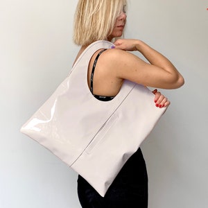 White patent leather shoulder bag is finished with an outside vertical zipper pocket and an adjustable strap. The bag is fully lined and has two inner pockets. The bag can be carried on the shoulder or crossbody. Height 19 Width 17 inches.