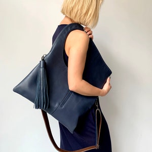 Blue leather shoulder bag with bronze leather interior collar. It has an outside vertical zipped pocket, a tassel and an adjustable strap. The bag is fully lined and has two inner pockets. The bag can be carried either on a shoulder or crossbody.