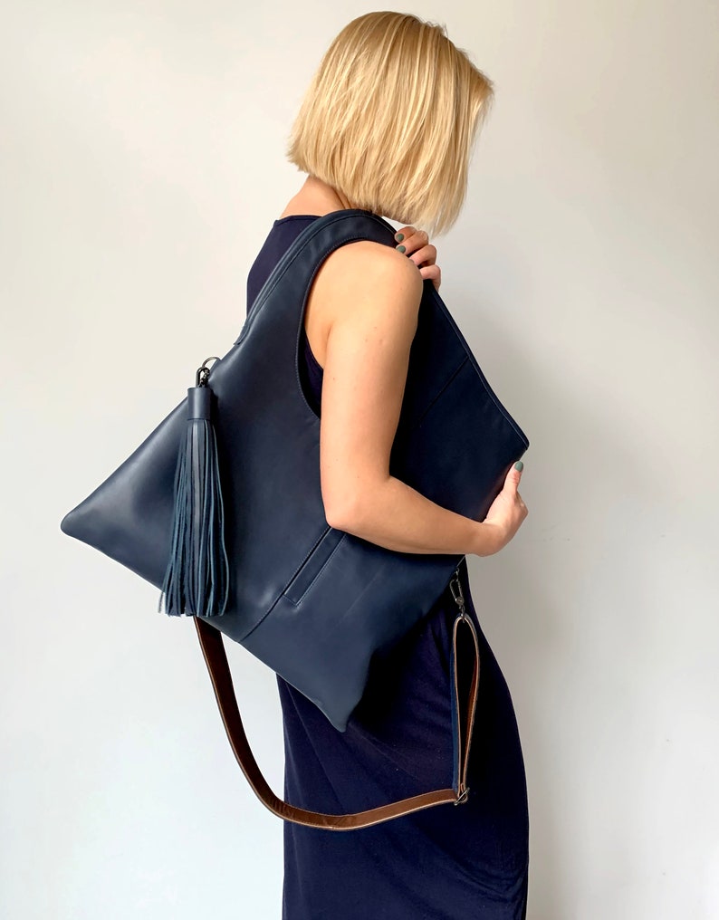 Blue leather shoulder bag with bronze leather interior collar. It has an outside vertical zipped pocket, a tassel and an adjustable strap. The bag is fully lined and has two inner pockets. The bag can be carried either on a shoulder or crossbody.