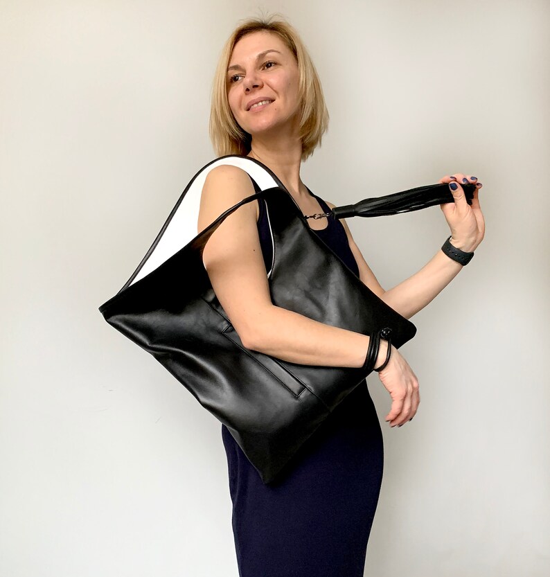 Black leather bag with white interior collar. Size: hight 19 width 17 inches. It is finished with an outside vertical zipper pocket and a tassel. The bag is fully lined and has two inner pockets.