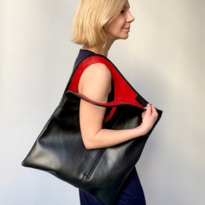 Black leather bag with red interior collar. Size: hight 19 width 17 inches. It is finished with an outside vertical zipper pocket. The bag is fully lined and has two inner pockets. The bag can be carried either on a shoulder or as a foldover clutch.