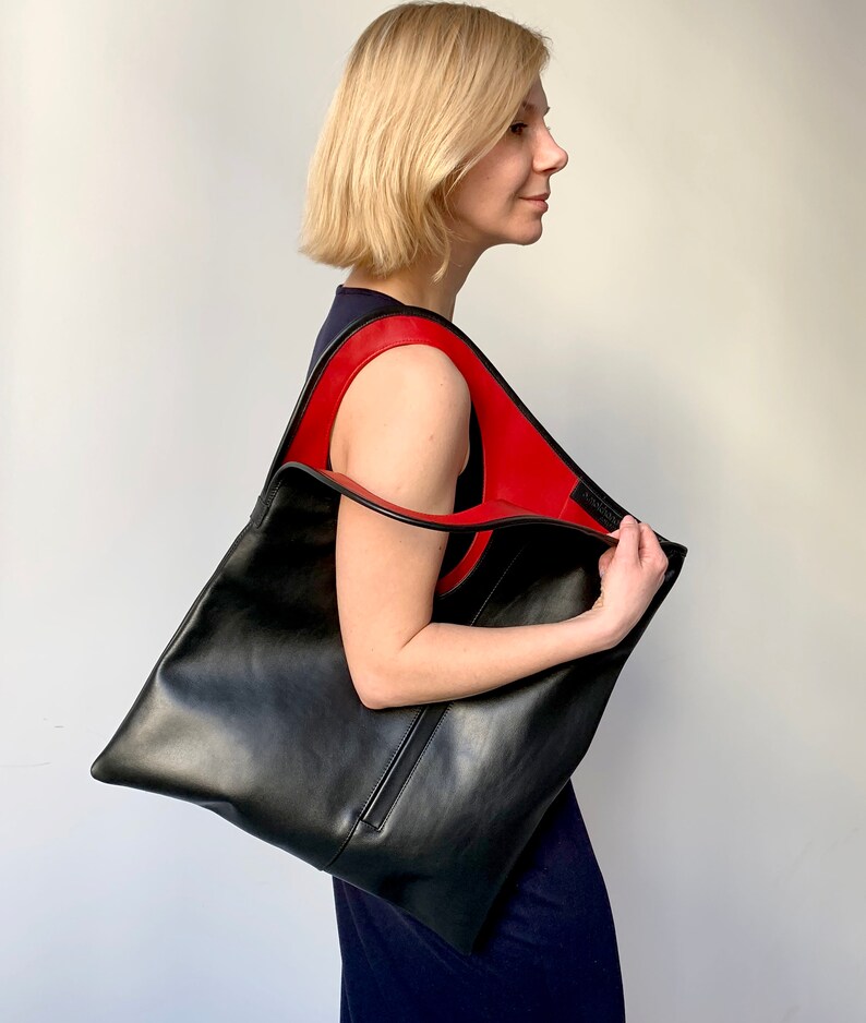 Black leather bag with red interior collar. Size: hight 19 width 17 inches. It is finished with an outside vertical zipper pocket. The bag is fully lined and has two inner pockets. The bag can be carried either on a shoulder or as a foldover clutch.