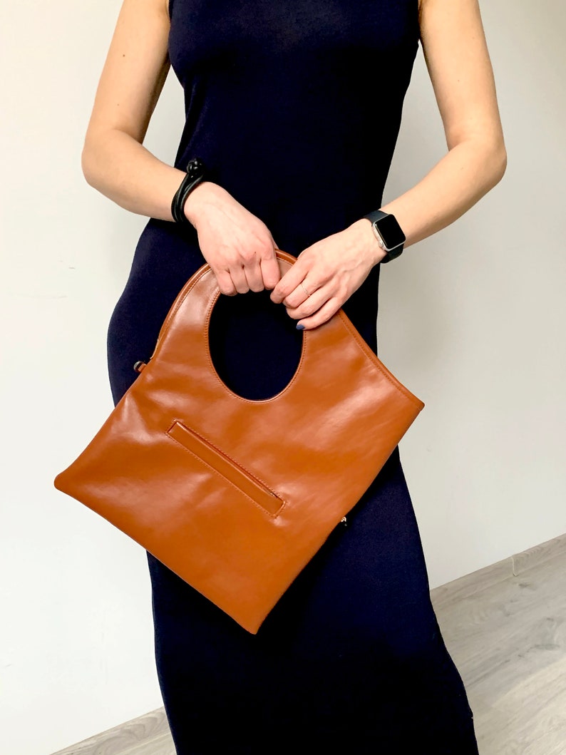 Cognac leather shoulder bag  is finished with an outside zipper pocket. The bag is fully lined and has two inner pockets. The bag can be carried on the shoulder or as a clutch. Height 15 Width 13.5 inches.