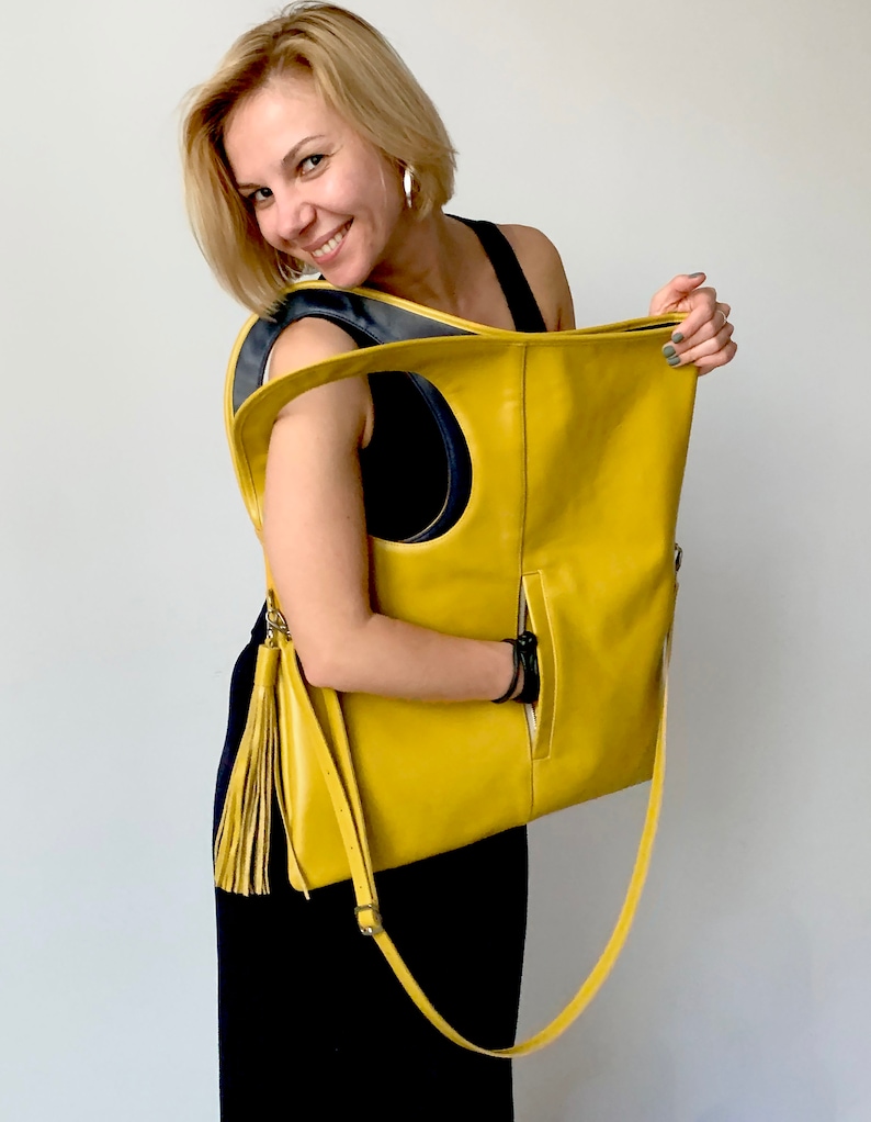 Yellow leather bag is finished with an outside vertical zipper pocket and a strap. The bag is fully lined and has two inner pockets. The bag can be carried on the shoulder or crossbody. Height 20.5 Width 18.5 inches.