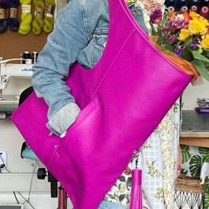 Black leather bag is finished with an outside vertical zipper pocket and a strap. The bag is fully lined and has two inner pockets. The bag can be carried on the shoulder or crossbody. Height 22 Width 20 inches.