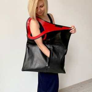 Black leather bag is finished with an outside vertical zipper pocket and a strap. The bag is fully lined and has two inner pockets. The bag can be carried on the shoulder or crossbody. Height 22 Width 20 inches.