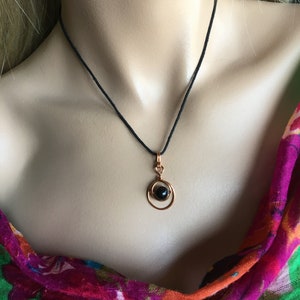 May include: A black gemstone pendant necklace with a copper wire design. The necklace is on a black cord.