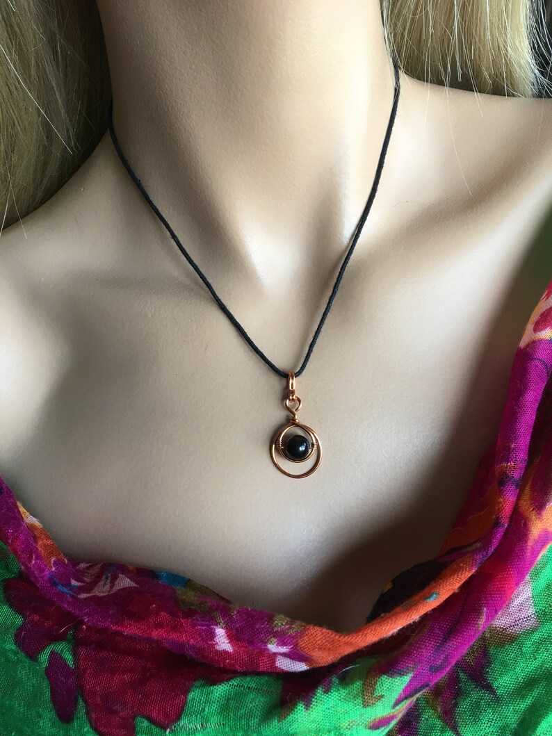 May include: A black gemstone pendant necklace with a copper wire design. The necklace is on a black cord.