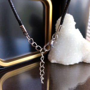 May include: A black leather cord necklace with a silver chain extender and lobster clasp.
