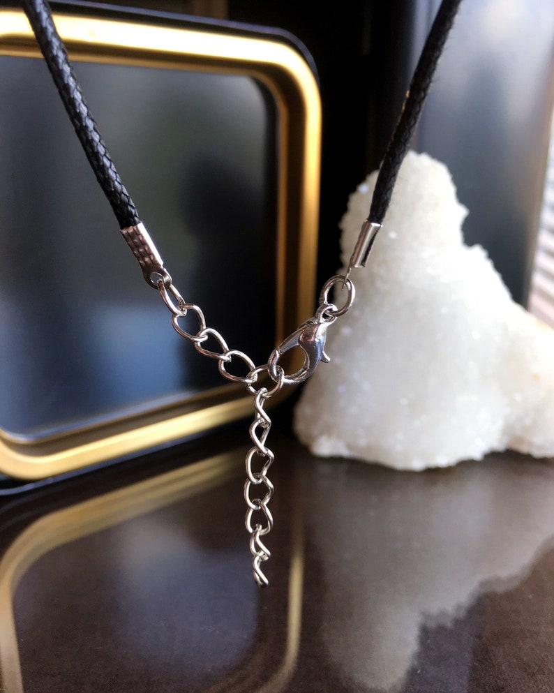 May include: A black leather cord necklace with a silver chain extender and lobster clasp.