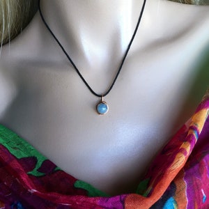 May include: A delicate necklace with a small, light blue gemstone pendant on a black cord.