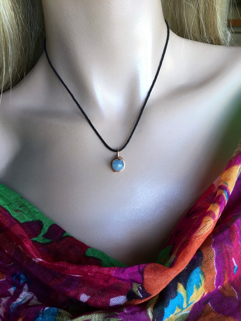 May include: A delicate necklace with a small, light blue gemstone pendant on a black cord.