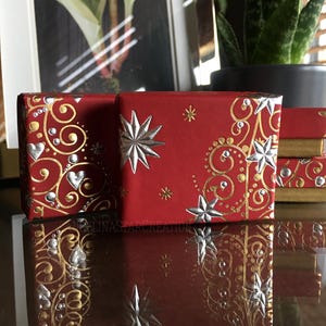 Peut inclure: Boîtes cadeaux rouges avec des accents décoratifs argentés et dorés, notamment des étoiles et des motifs tourbillonnants. Les boîtes sont disposées sur une surface réfléchissante, créant un effet miroir. Le thème général est festif et célébratif.