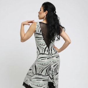 May include: Sleeveless dress with a black, white, and light green abstract pattern. The dress features a sheer black panel on the upper back and a black trim at the hem. The model is wearing high-heeled sandals.