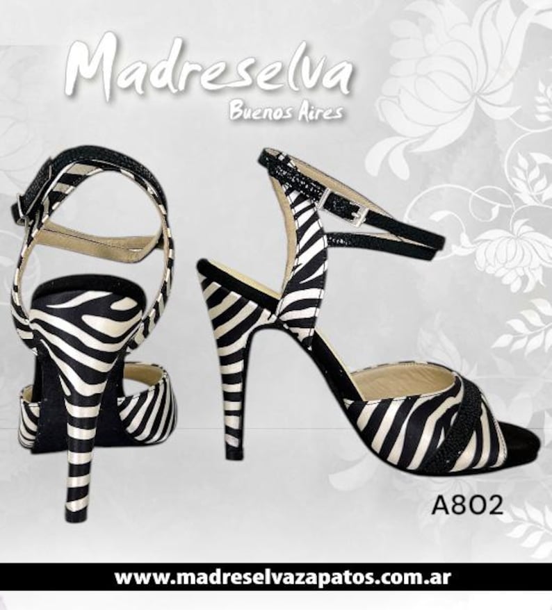 May include: Two high-heeled sandals with a zebra stripe pattern in black and white. The sandals have a thin ankle strap and a buckle closure. The heels are stiletto style. The text "Madreselva Buenos Aires" is at the top.