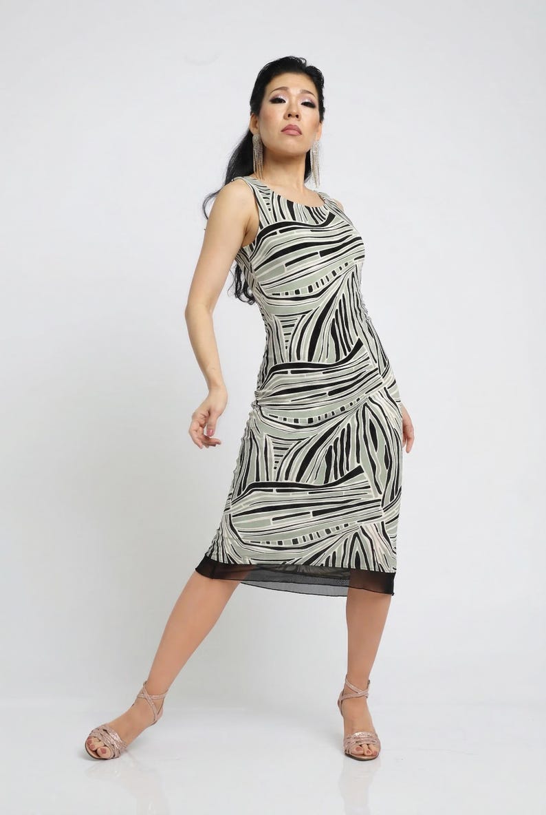 May include: Sleeveless midi dress with a black, white, and gray abstract pattern. The dress has a black mesh hem and is paired with strappy sandals. The model is standing in a studio setting.