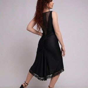 May include: Black sleeveless dress with a sheer back panel and lace trim at the hem. The dress has a fitted bodice and a flowing skirt. The model is wearing black high heels.